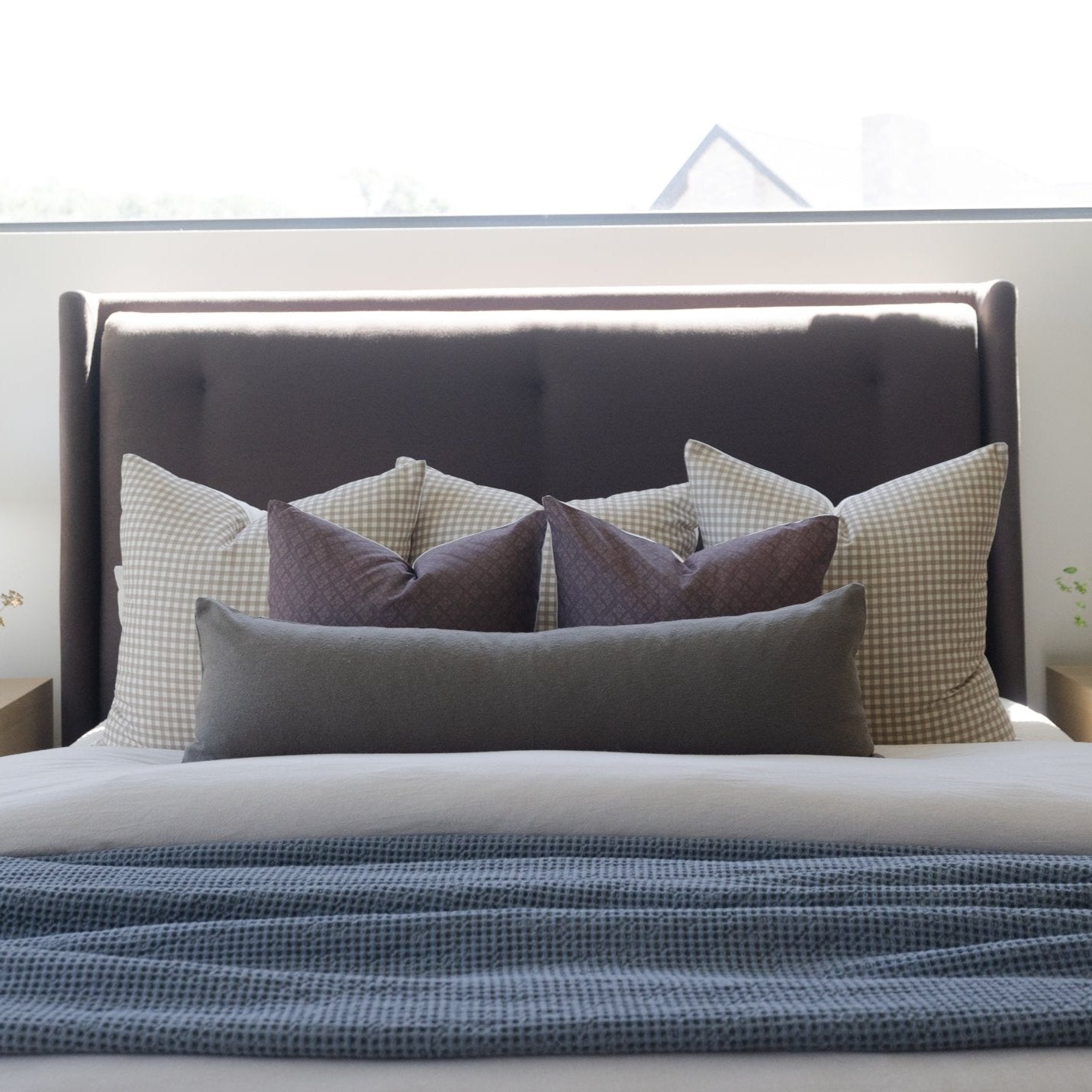 Tan and white gingham patterned pillows arranged on a dark upholstered bed headboard.