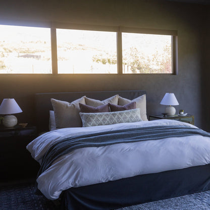 Maroon throw blanket draped across a bed with patterned pillows and white bedding.