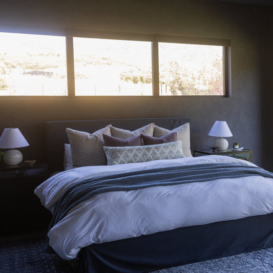 Maroon throw blanket draped across a bed with patterned pillows and white bedding.