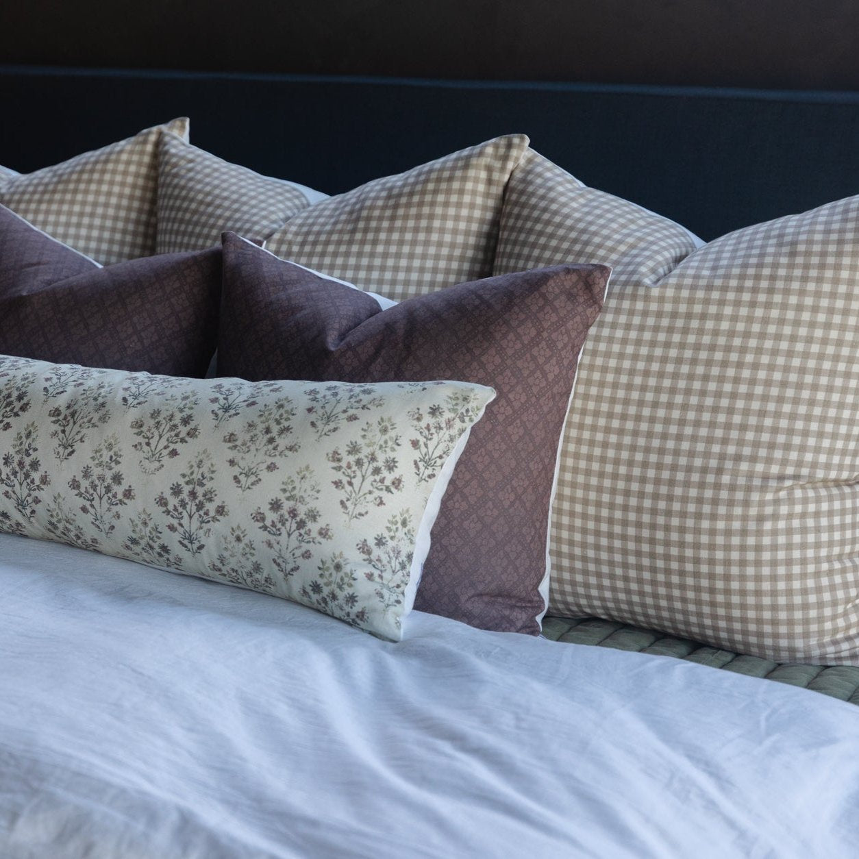 Maroon and cream patterned decorative pillows arranged on a bed with white linens.