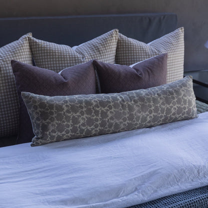 Maroon lumbar pillow arranged with gingham and patterned pillows on a bed with blue bedding.