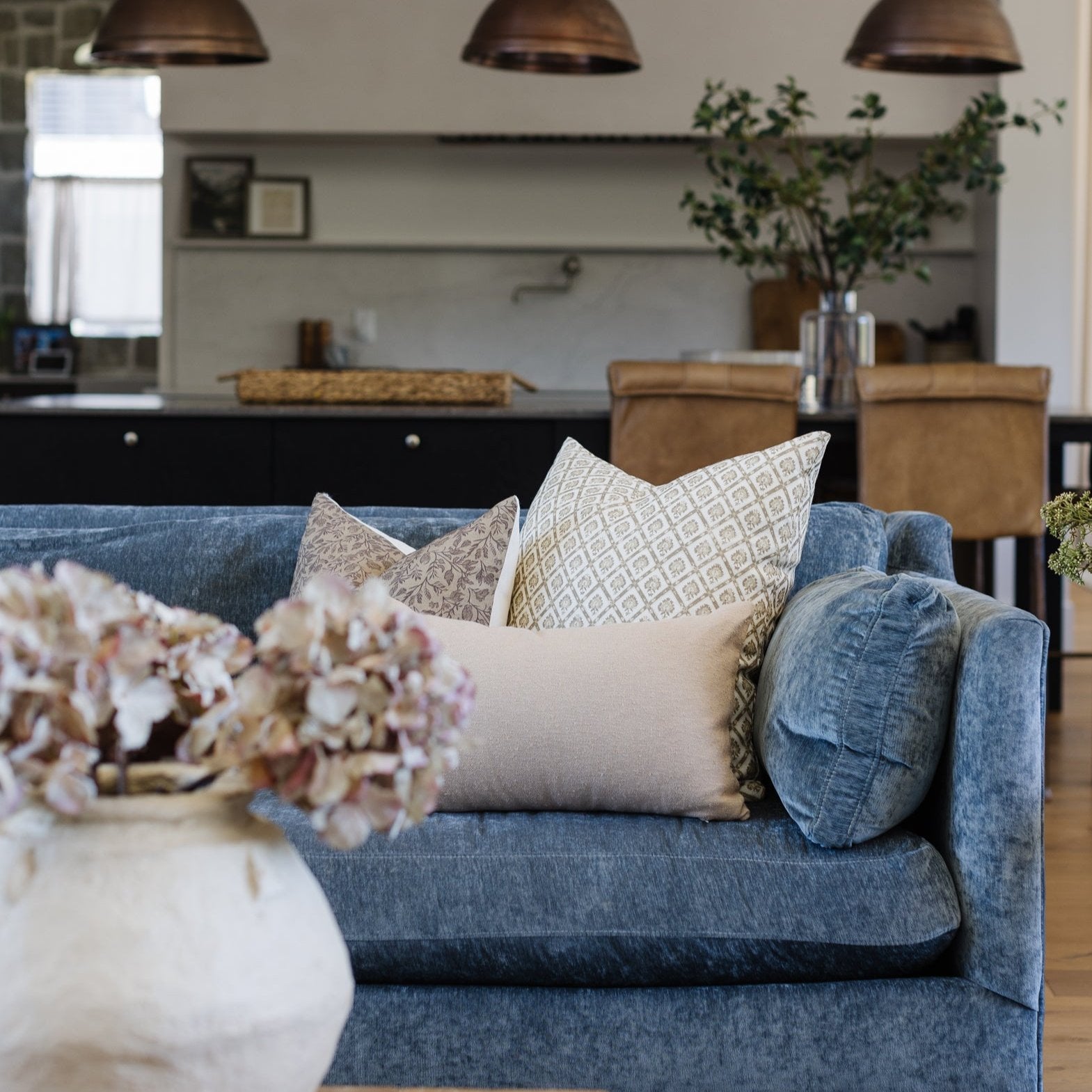 Blue linen sofa with decorative pillows in neutral tones and geometric patterns in modern living room setting.