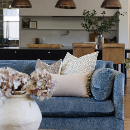 Blue linen sofa with decorative pillows in neutral tones and geometric patterns in modern living room setting.