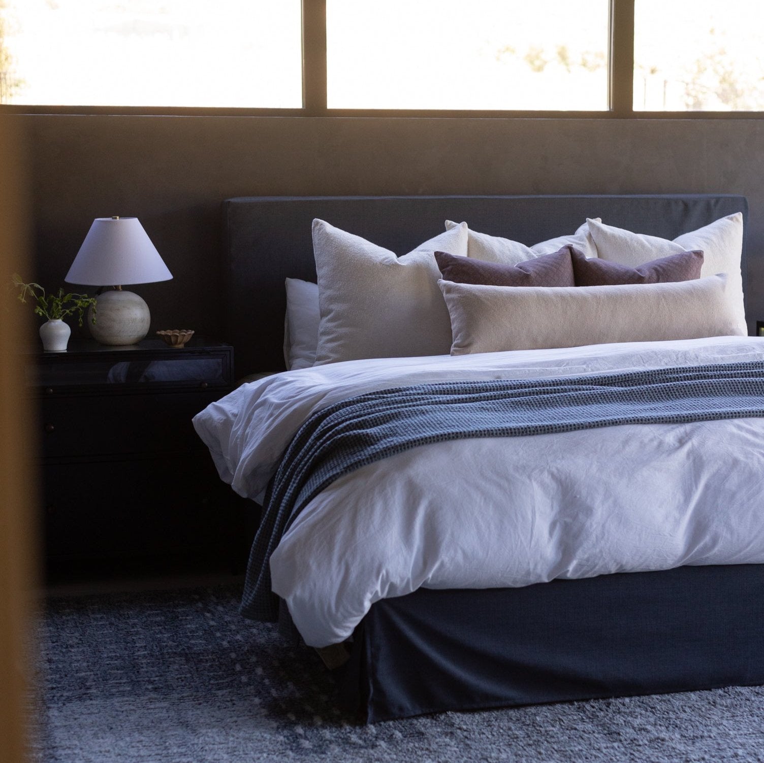 Beige boucle rectangular pillows arranged on a dark upholstered bed with white and striped bedding.