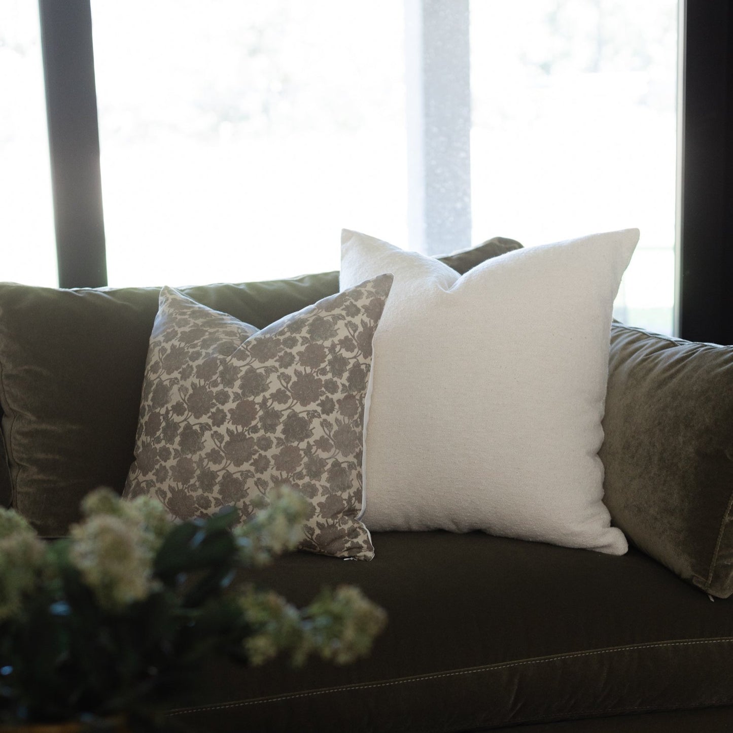 Cream and patterned throw pillows arranged on a dark sofa near a window.