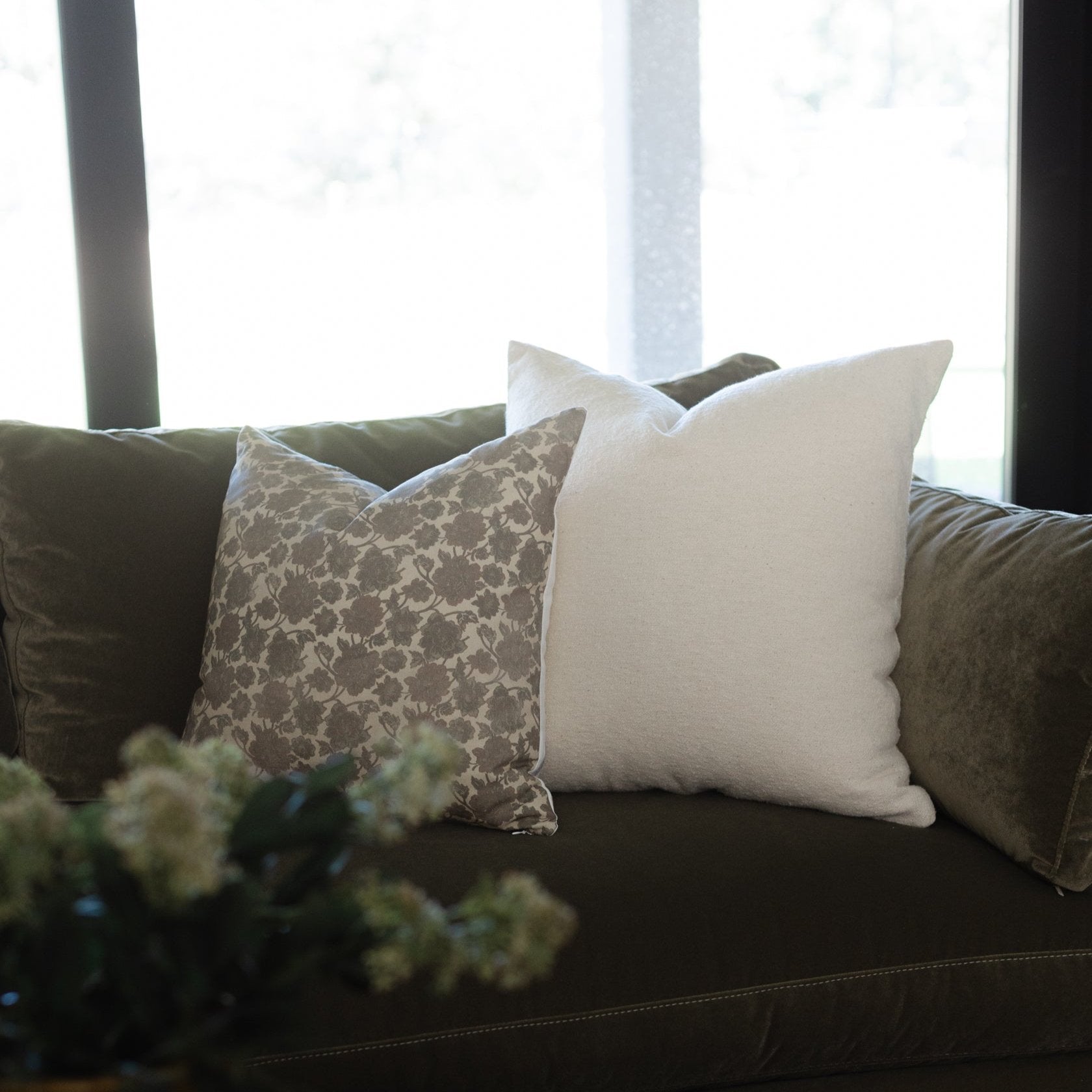 Cream and patterned throw pillows arranged on a dark sofa near a window.