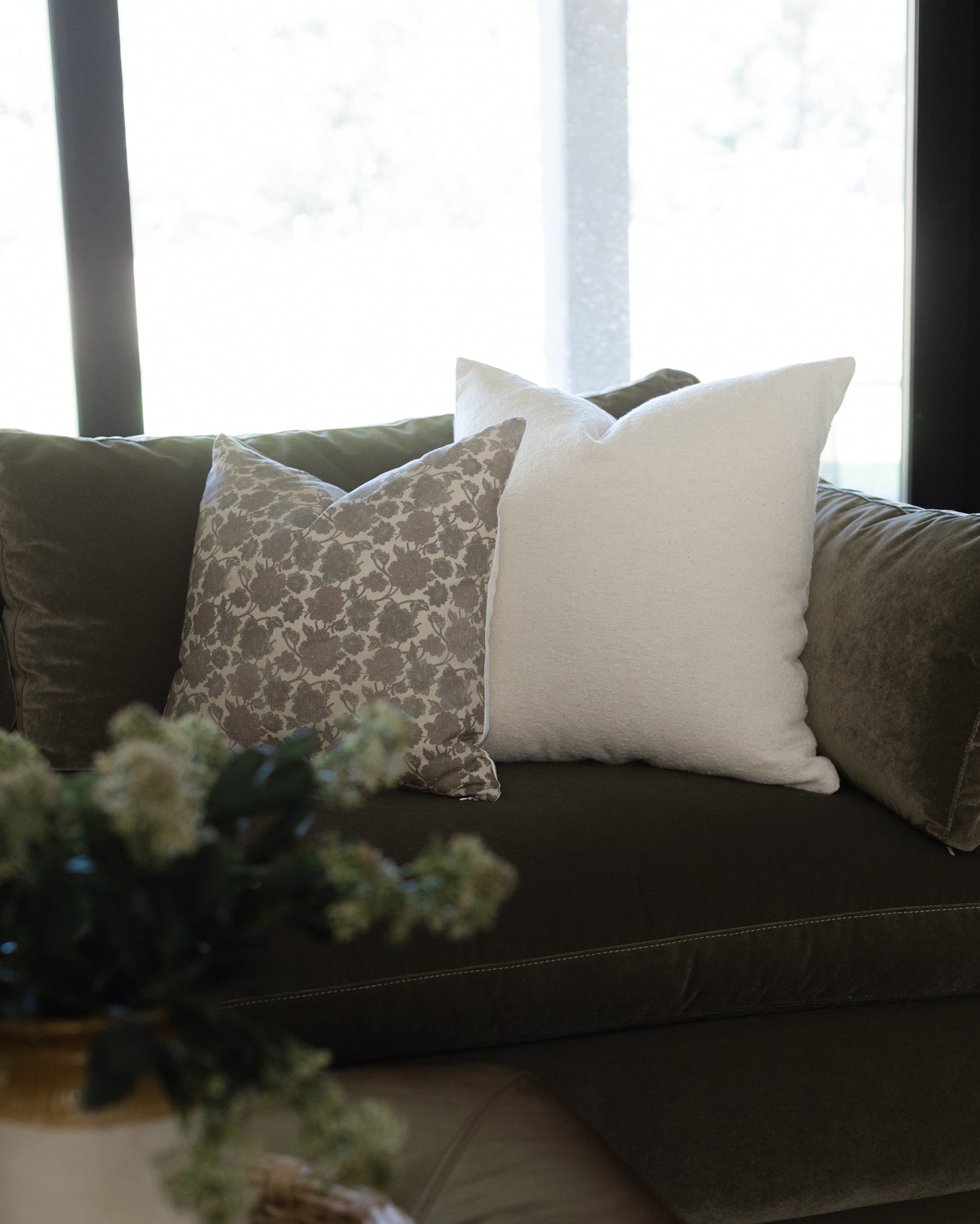 Off-white boucle throw pillow with textured weave displayed on dark sofa between patterned cushions.