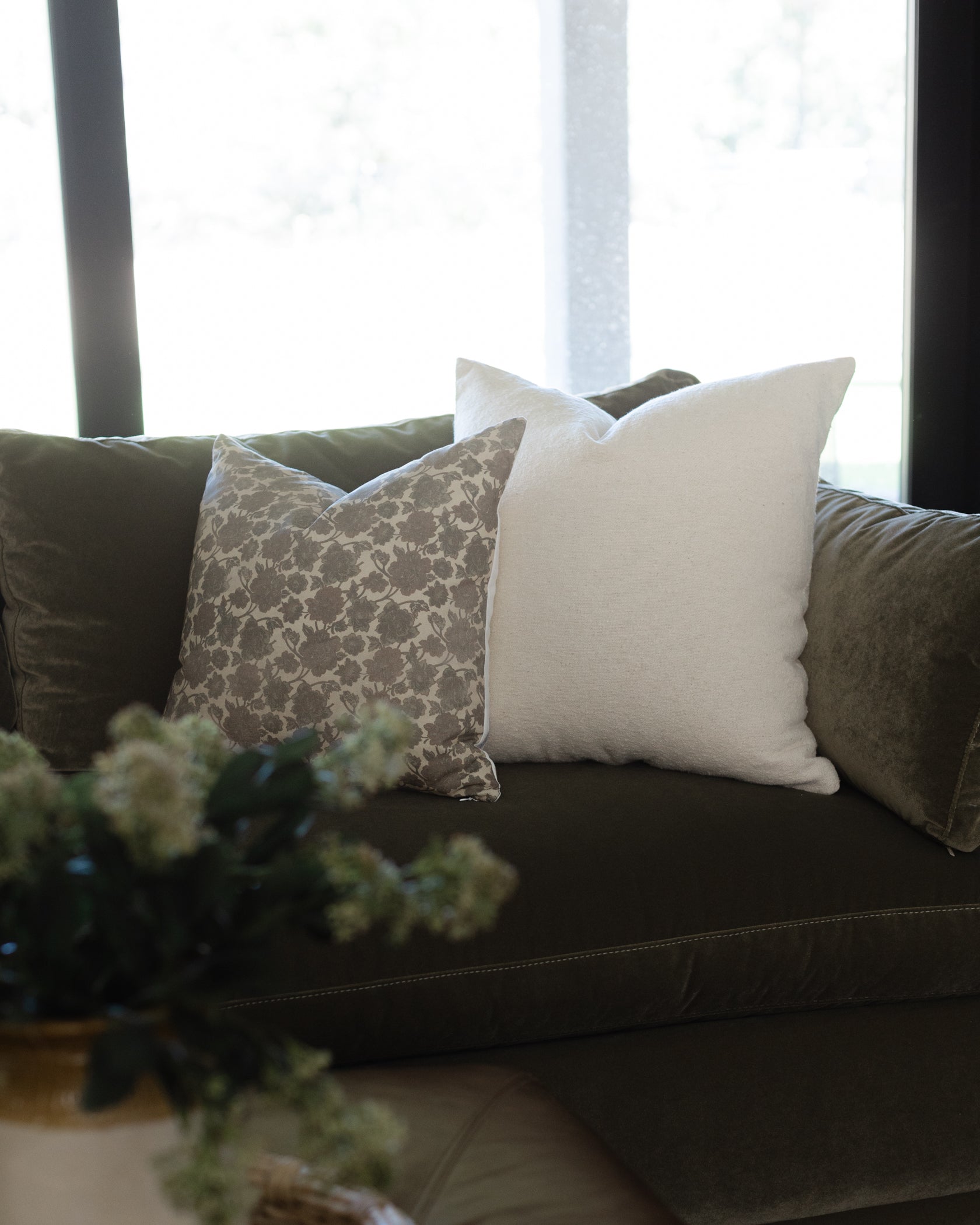 Off-white boucle throw pillow with textured weave displayed on dark sofa between patterned cushions.