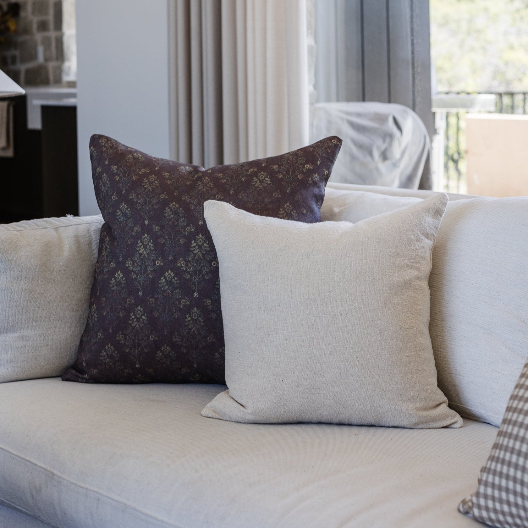 Dark burgundy linen pillow with tonal damask pattern displayed on cream sofa with neutral pillows.