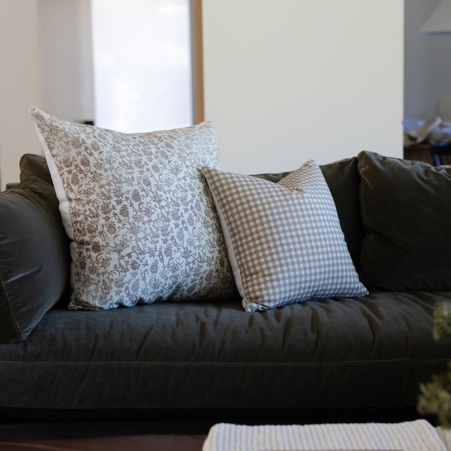 Two decorative pillows with damask and gingham patterns displayed on a dark gray sofa.