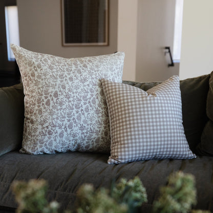 Two decorative pillows on a dark sofa: one with tan floral damask pattern and one with tan gingham check pattern.