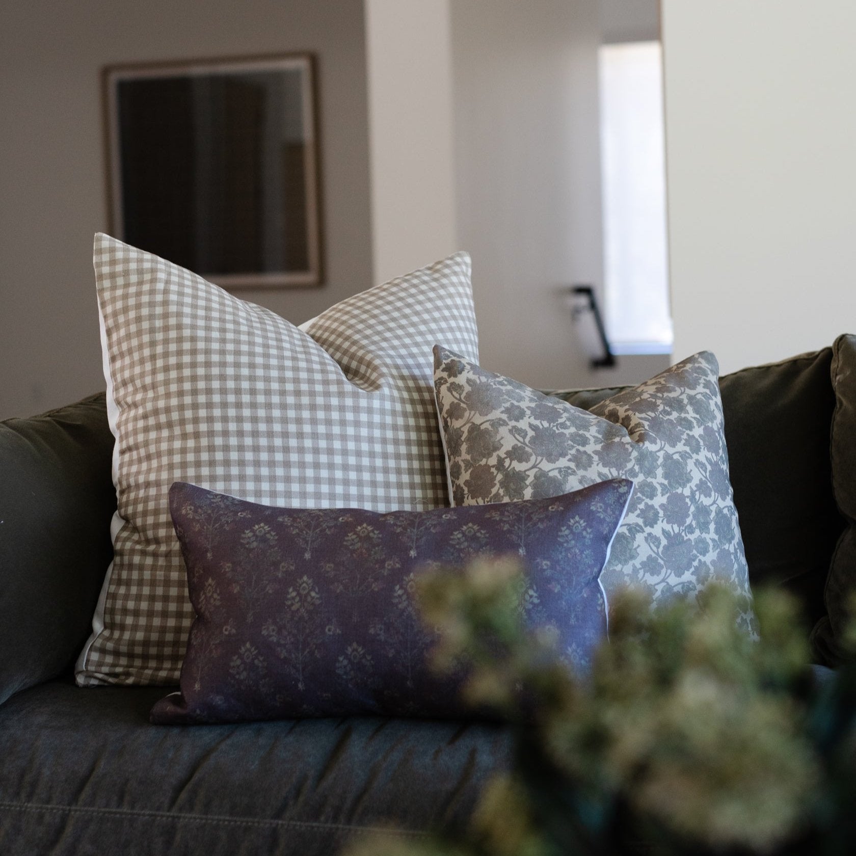 Three decorative pillows in gingham, floral, and damask patterns arranged on a dark sofa.