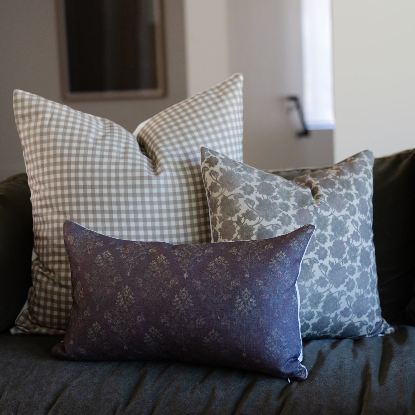 Three decorative pillows in coordinating patterns: beige gingham, blue floral damask, and burgundy floral designs arranged on