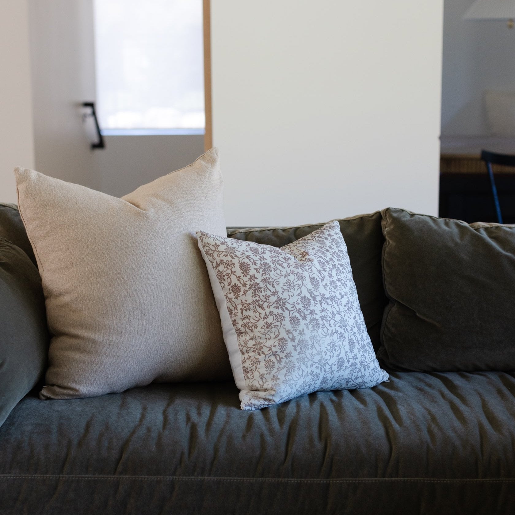 Three decorative pillows in cream, patterned tan and white, and dark olive on a dark gray upholstered sofa.