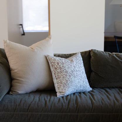 Three decorative pillows in cream, patterned tan and white, and dark olive on a dark gray upholstered sofa.