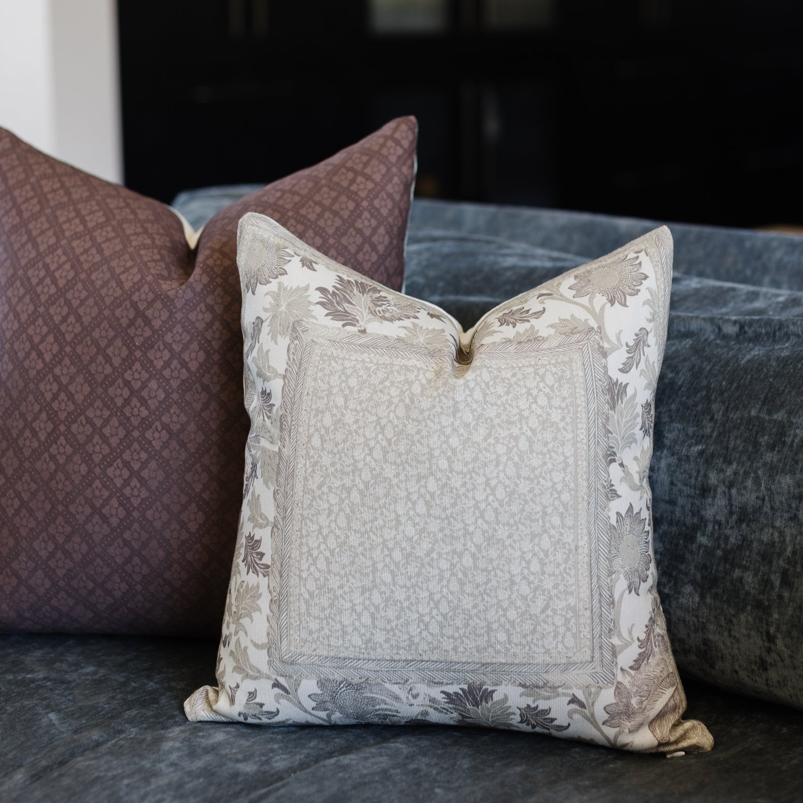 Cream pillow with gray botanical border pattern and textured center panel, displayed with coordinating corduroy pillows on gr
