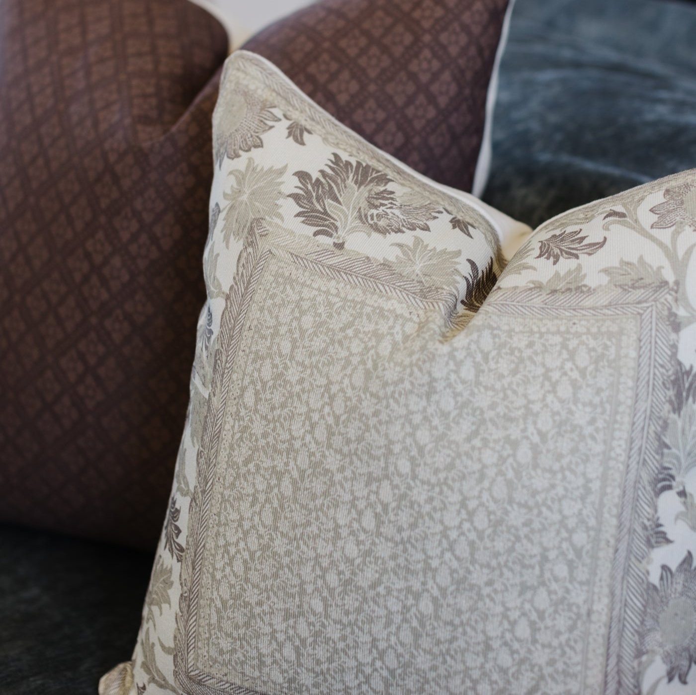 Cream and taupe botanical patterned pillow with leaf motifs resting against brown corduroy furniture.
