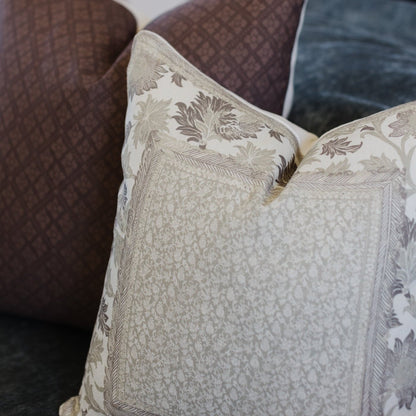 Cream and taupe botanical patterned pillow with leaf motifs resting against brown corduroy furniture.