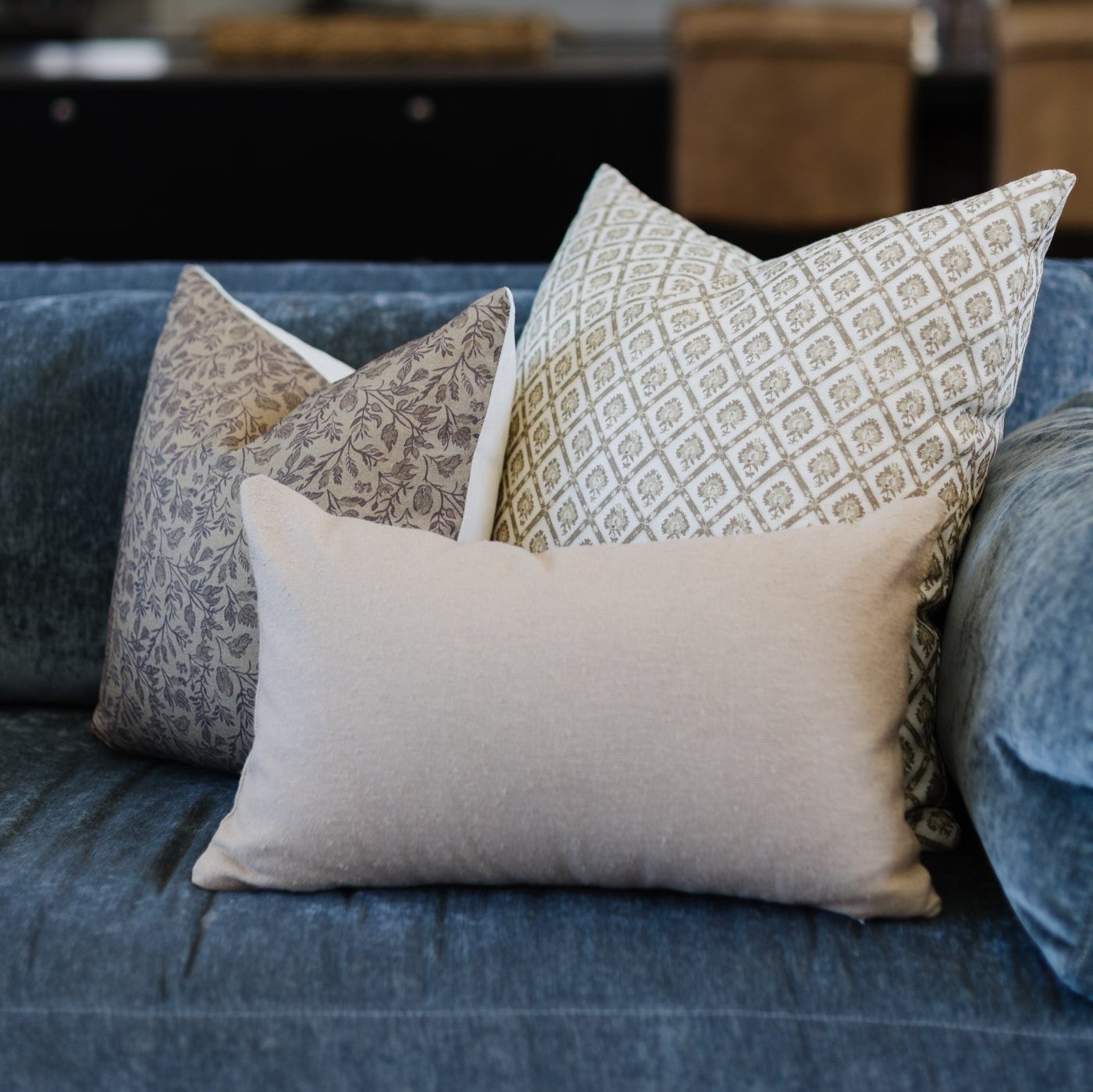 Three linen pillows with geometric and floral patterns displayed on a blue upholstered sofa.