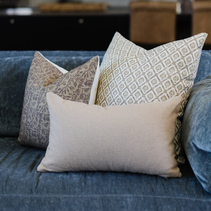 Three linen pillows with geometric and floral patterns displayed on a blue upholstered sofa.