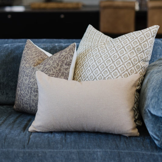 Three linen pillows with geometric and floral patterns displayed on a blue upholstered sofa.