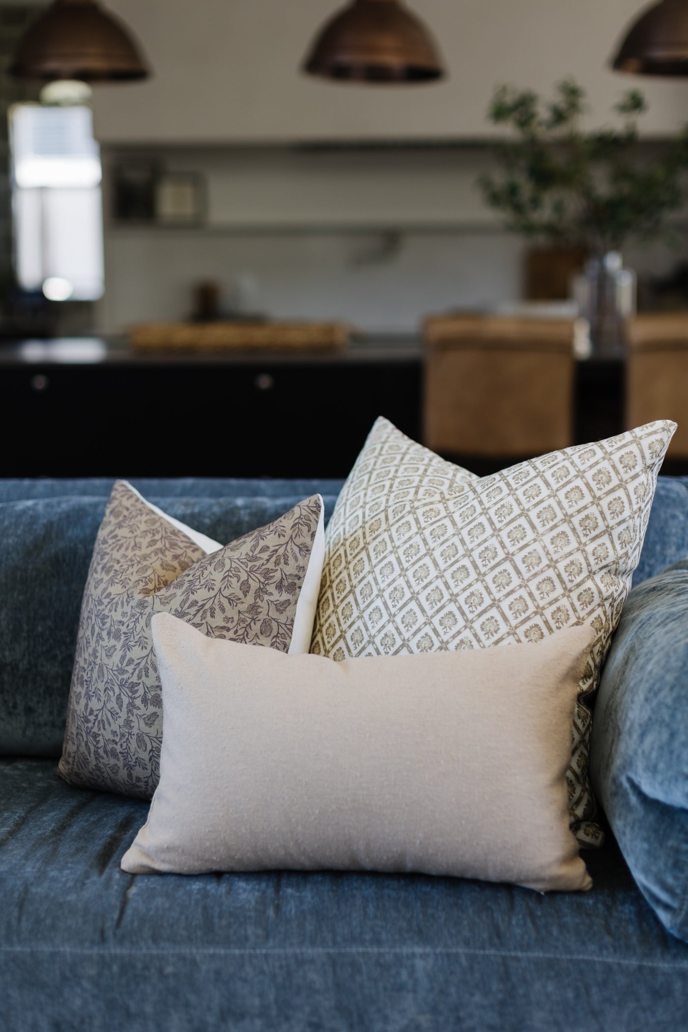 Beige boucle textured pillow with geometric and floral pattern variations displayed on a blue sofa.