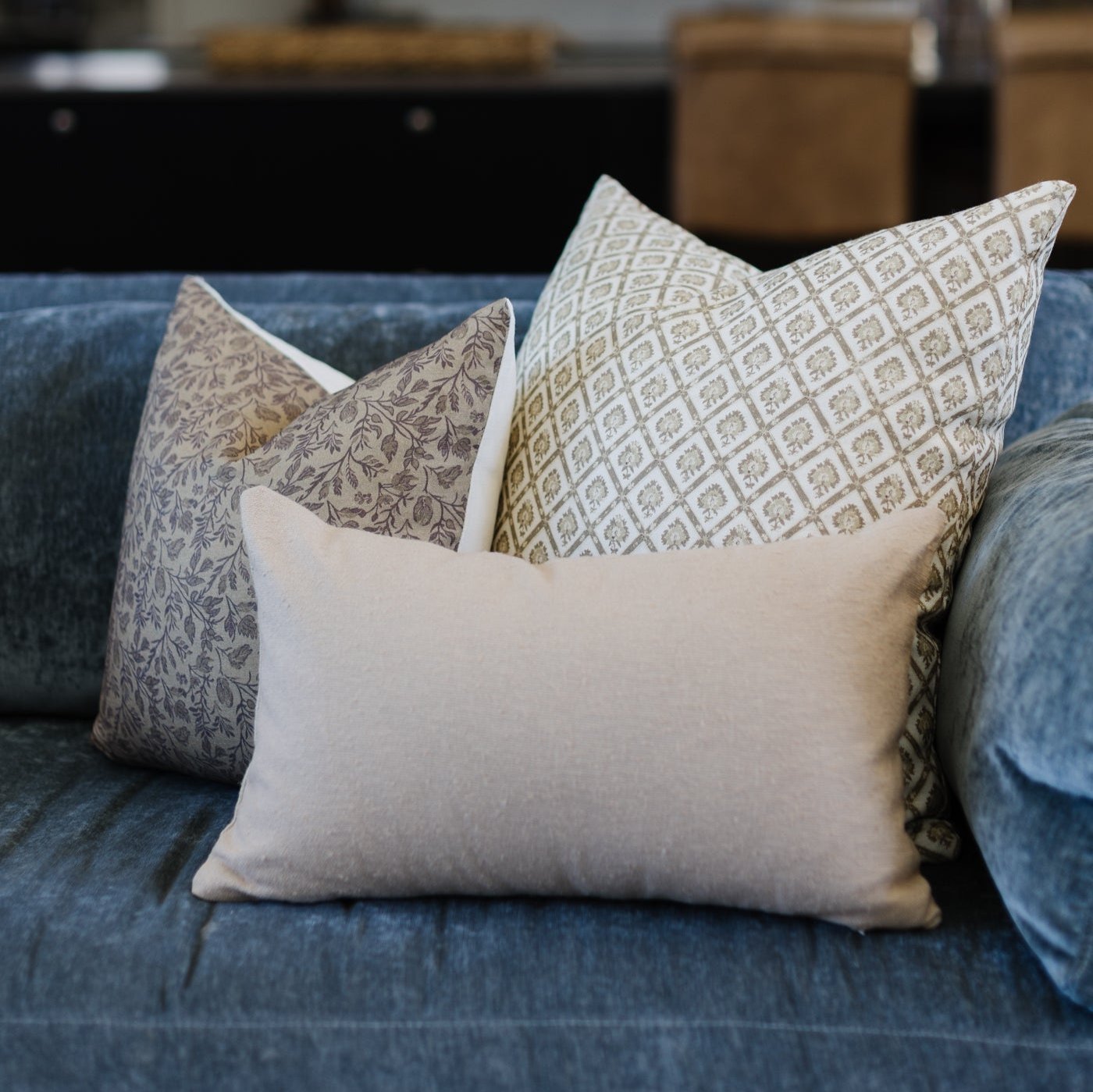 Three decorative pillows arranged on a blue upholstered sofa: one cream solid pillow in front with two patterned pillows behi