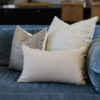 Three decorative pillows arranged on a blue upholstered sofa: one cream solid pillow in front with two patterned pillows behi