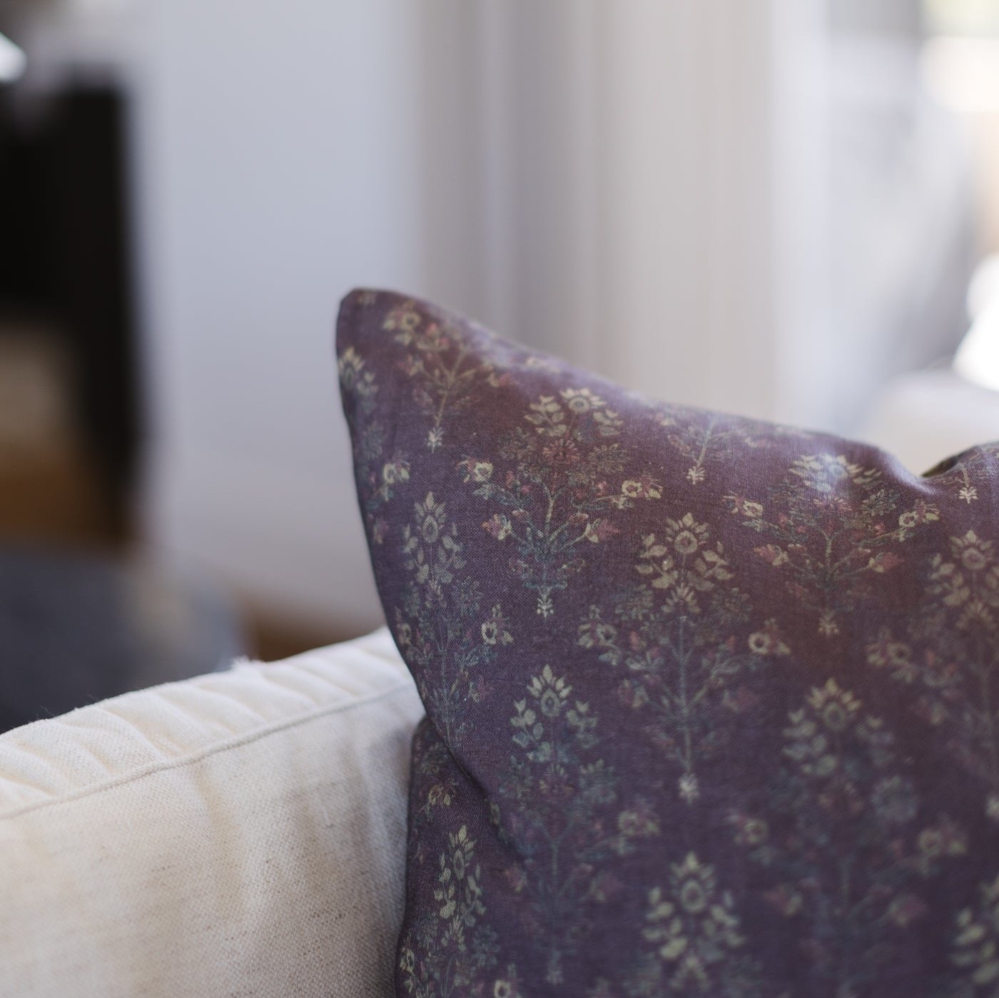 Deep burgundy linen pillow with cream floral damask pattern displayed on white upholstered furniture.