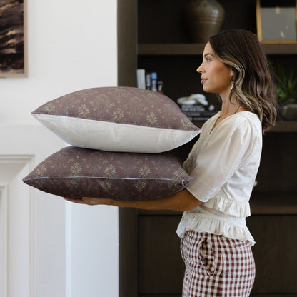 Two burgundy linen pillows with subtle damask pattern, one with cream back, stacked and held by woman indoors.