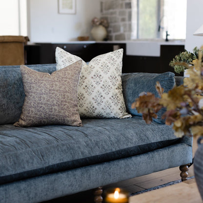 Afton decorative pillows in taupe and cream patterns displayed on a blue-gray sofa in a living room setting.