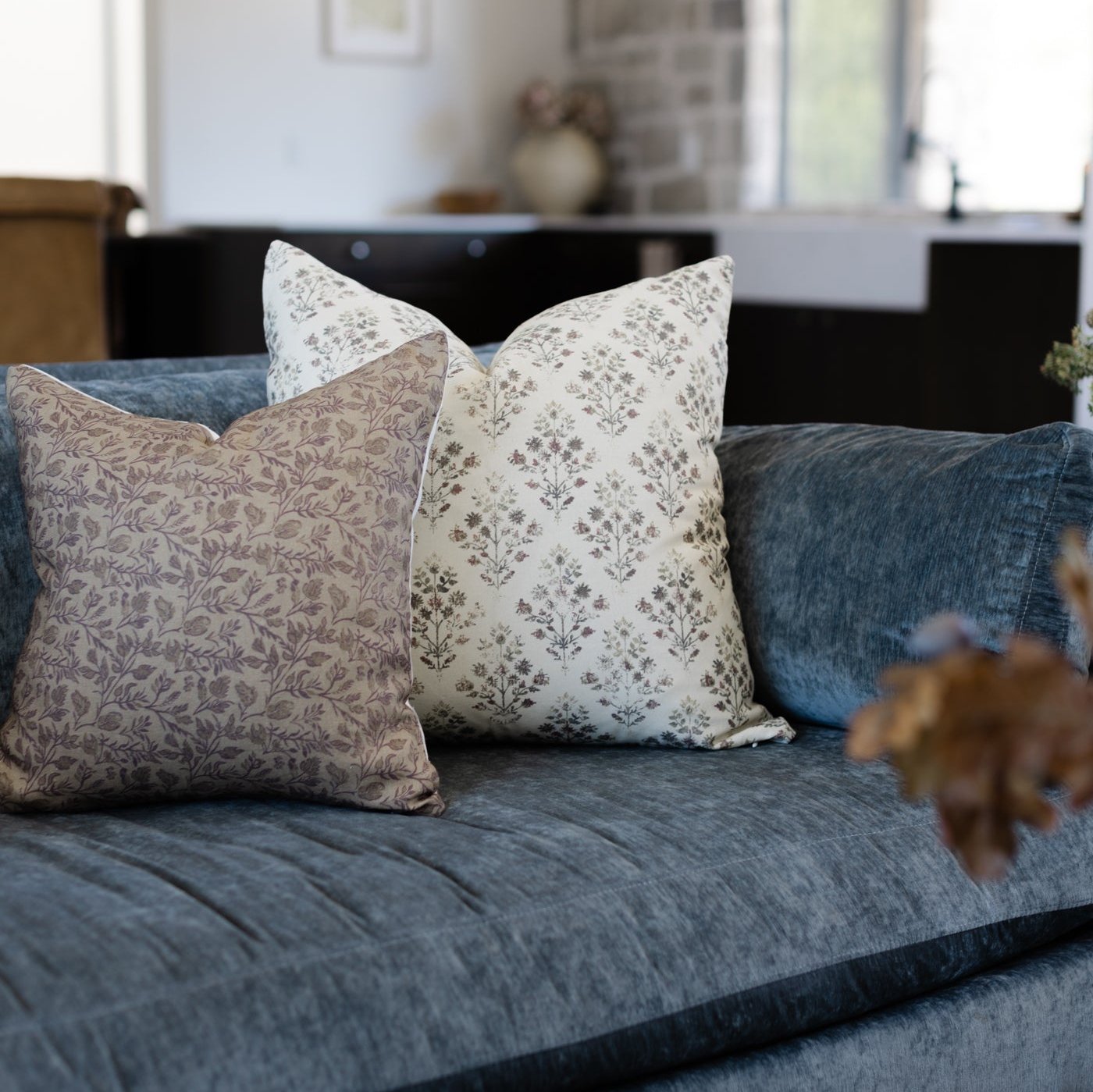 Decorative pillows with floral and botanical prints in taupe and cream on blue upholstered sofa.