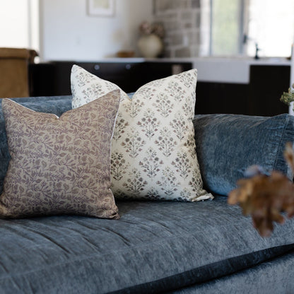 Decorative pillows with floral and botanical prints in taupe and cream on blue upholstered sofa.