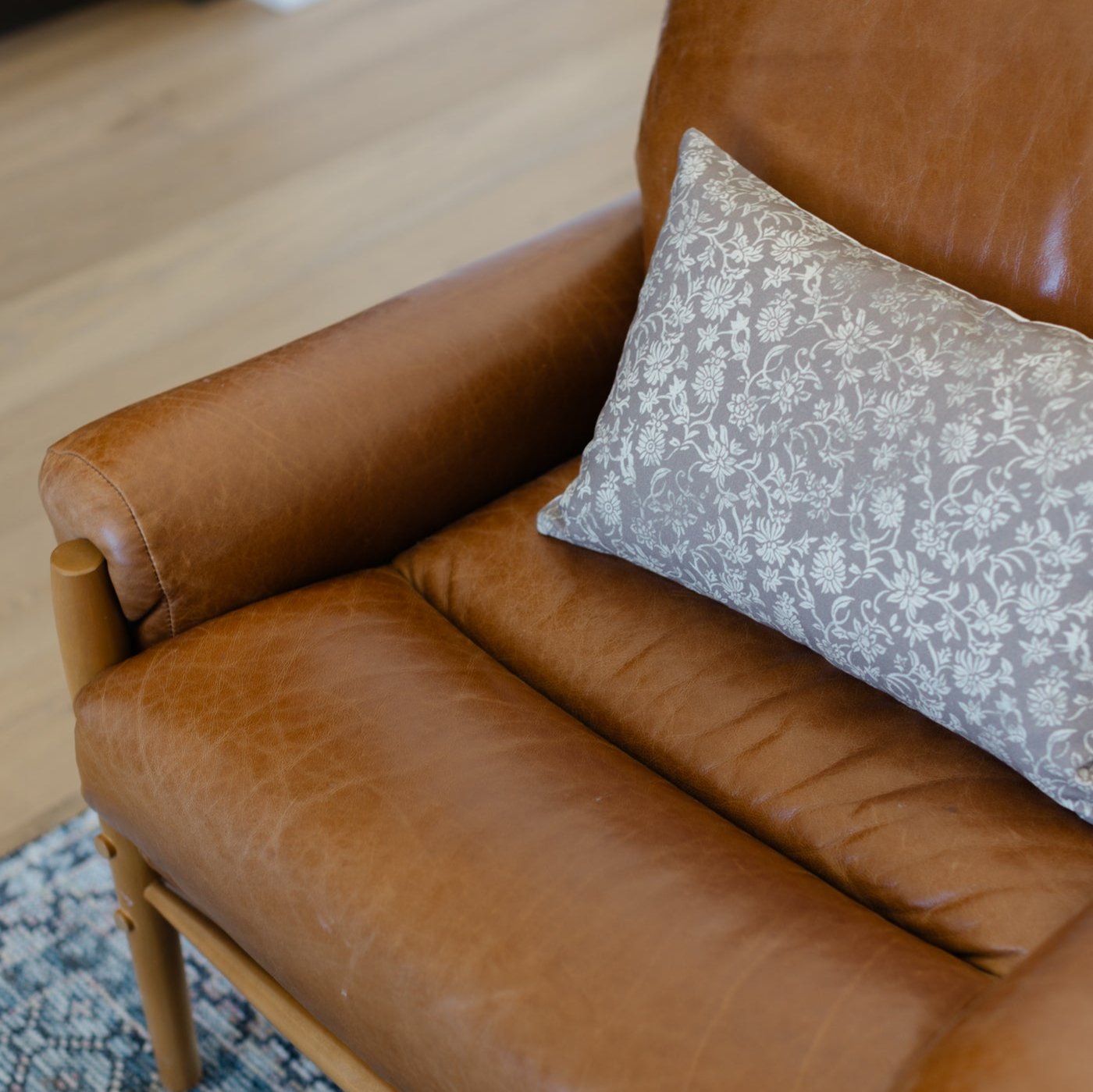 Gray and white damask patterned lumbar pillow placed on a tan leather armchair.