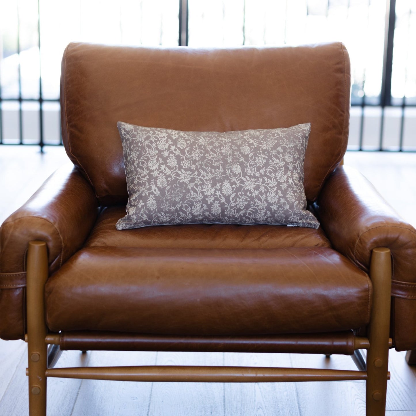 Gray damask patterned lumbar pillow displayed on a brown leather armchair.