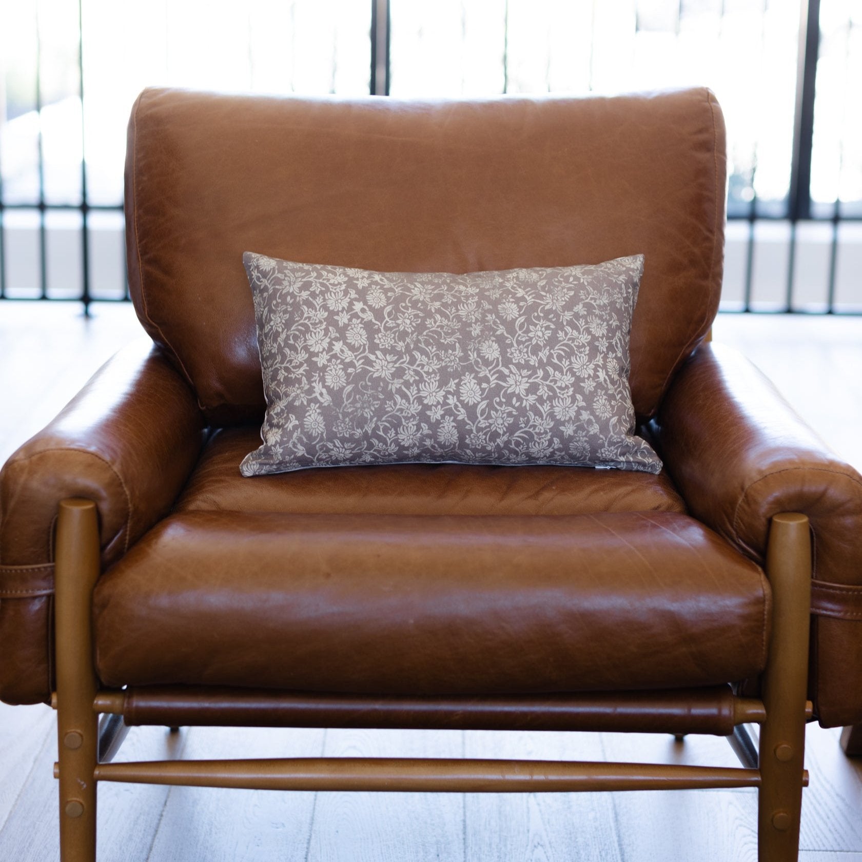 Gray damask patterned lumbar pillow displayed on a brown leather armchair.