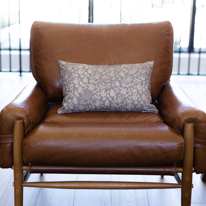 Gray damask patterned lumbar pillow displayed on a brown leather armchair.