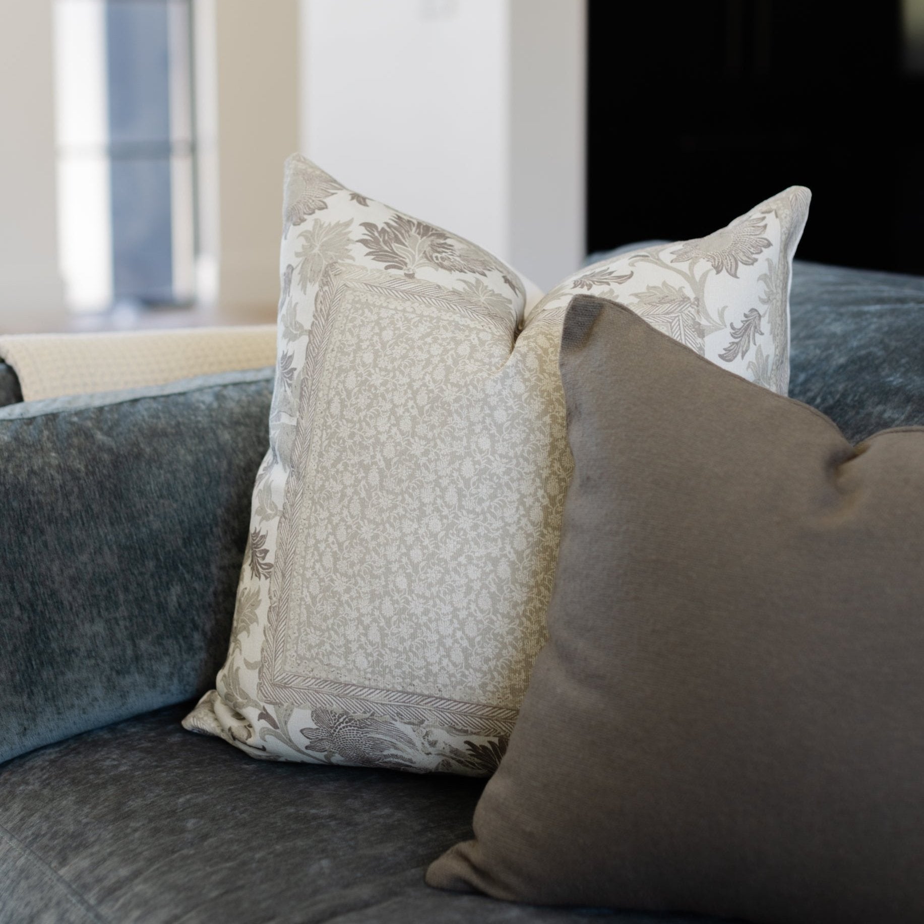 Juliette corduroy pillow with botanical print front and solid back, displayed on gray upholstered sofa.