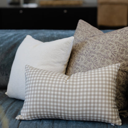 Tan and white gingham check lumbar pillow displayed on a blue upholstered sofa with coordinating pillows.