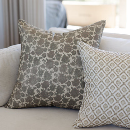 Two decorative pillows with floral and geometric patterns in taupe and cream on a neutral sofa.