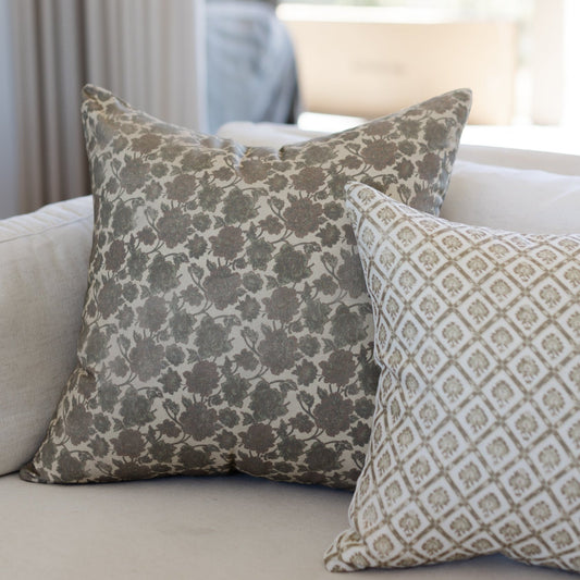 Two decorative pillows with floral and geometric patterns in taupe and cream on a neutral sofa.