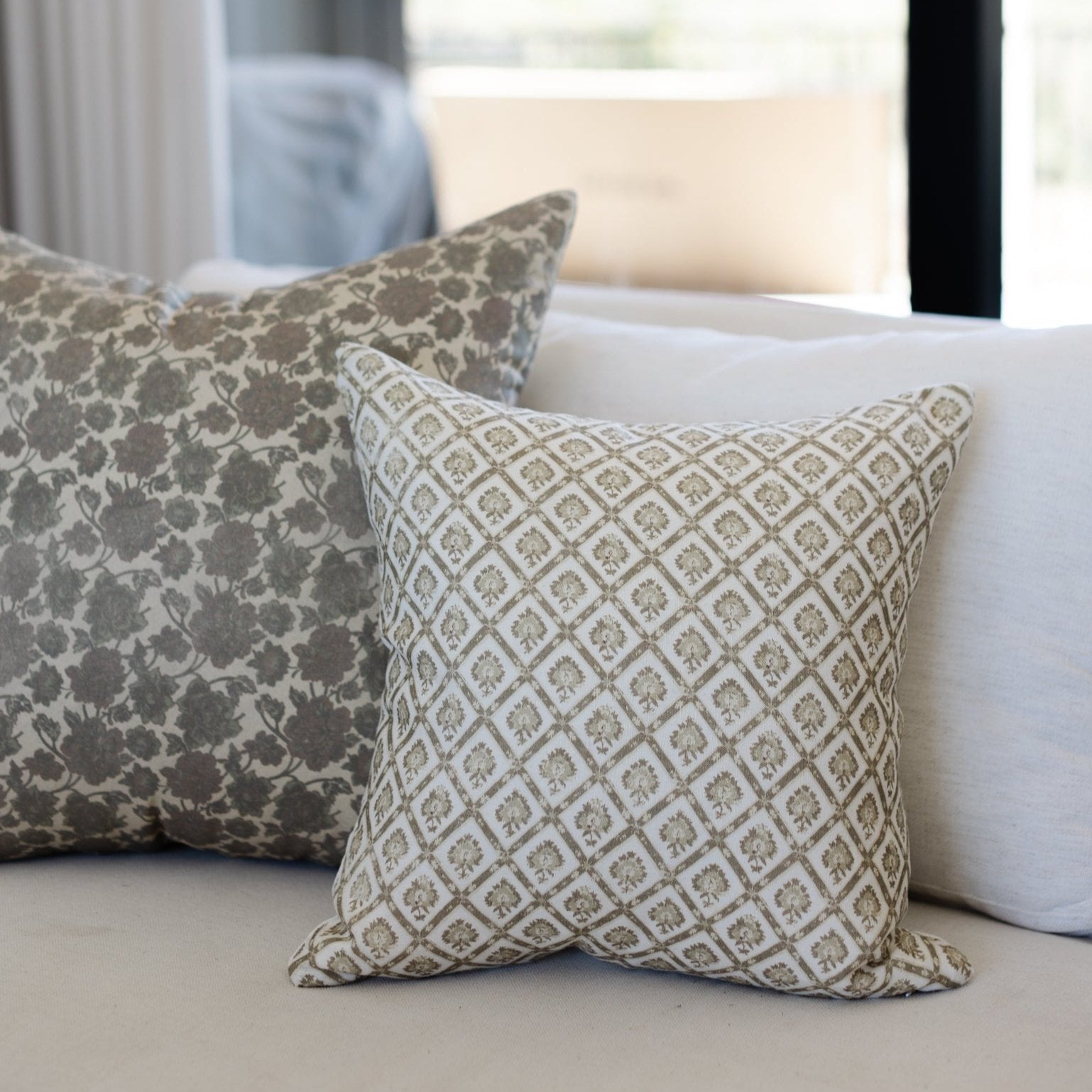 Decorative linen pillow with geometric diamond pattern in beige and cream, displayed on light sofa with floral patterned pill
