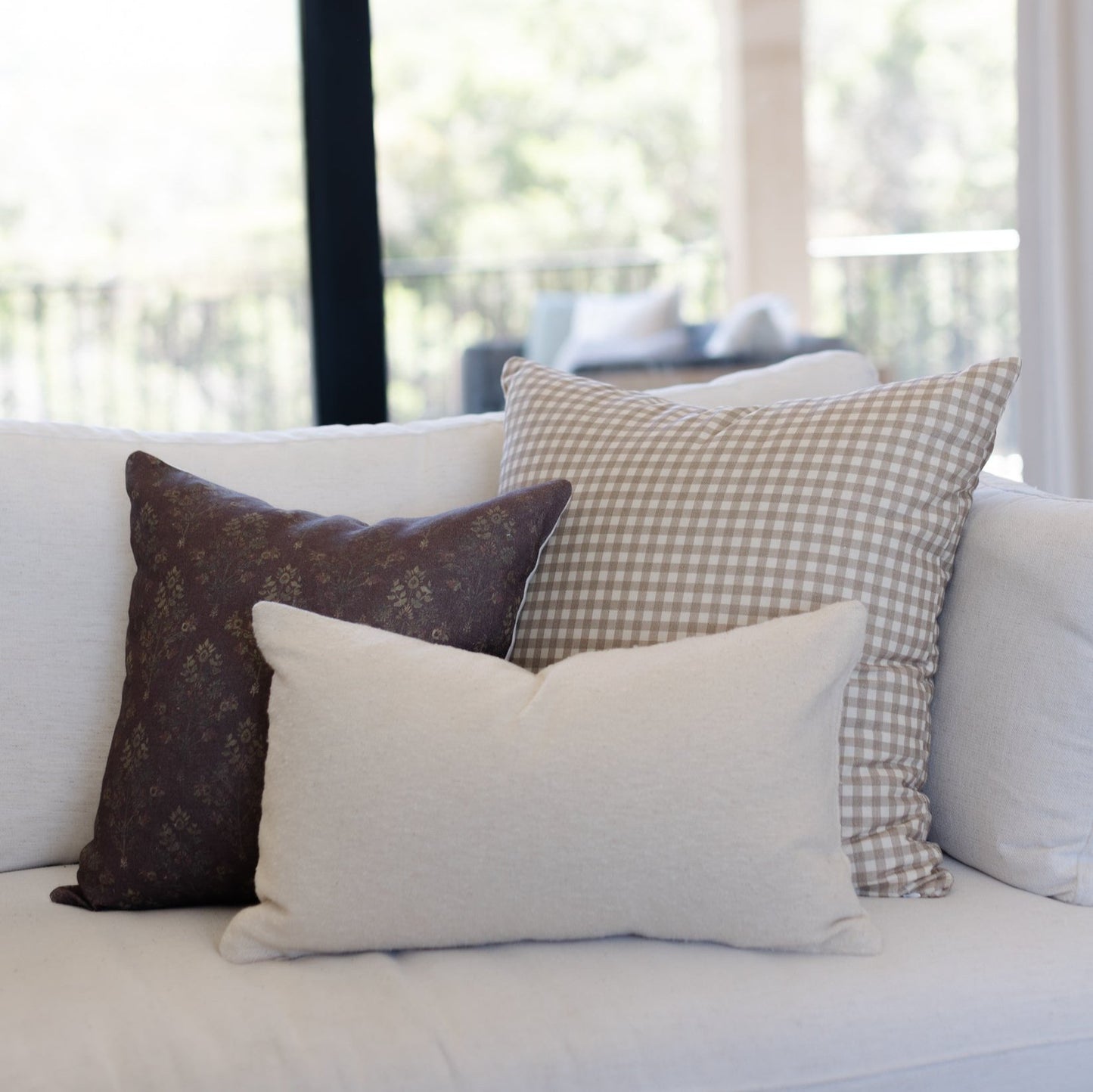 Tan gingham patterned pillow with small white checks displayed on a cream sofa.