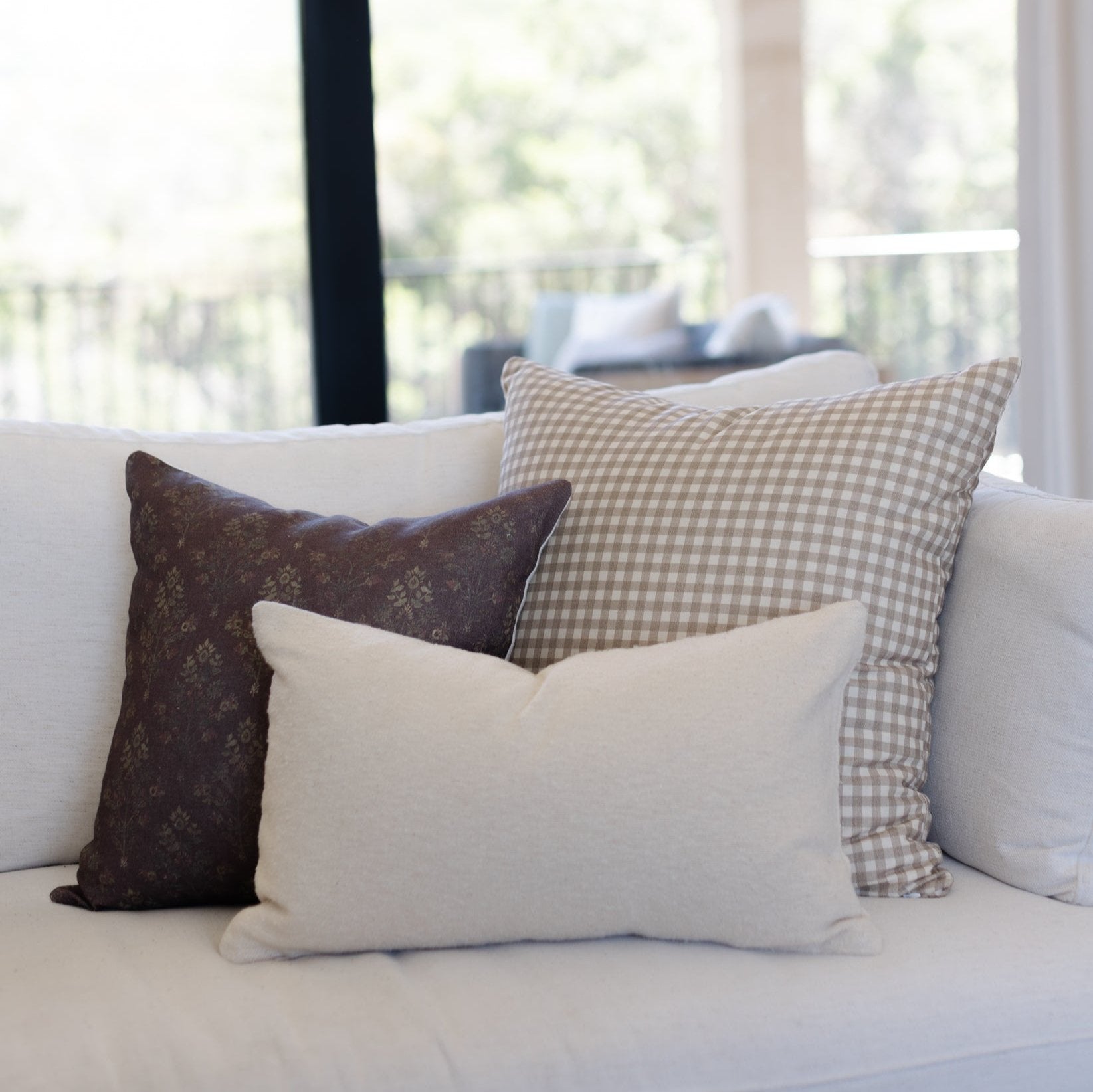 Tan gingham patterned pillow with small white checks displayed on a cream sofa.