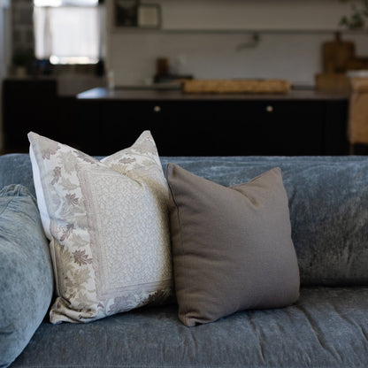 Blue-gray corduroy pillows arranged on a sofa, one with floral pattern and one solid taupe.