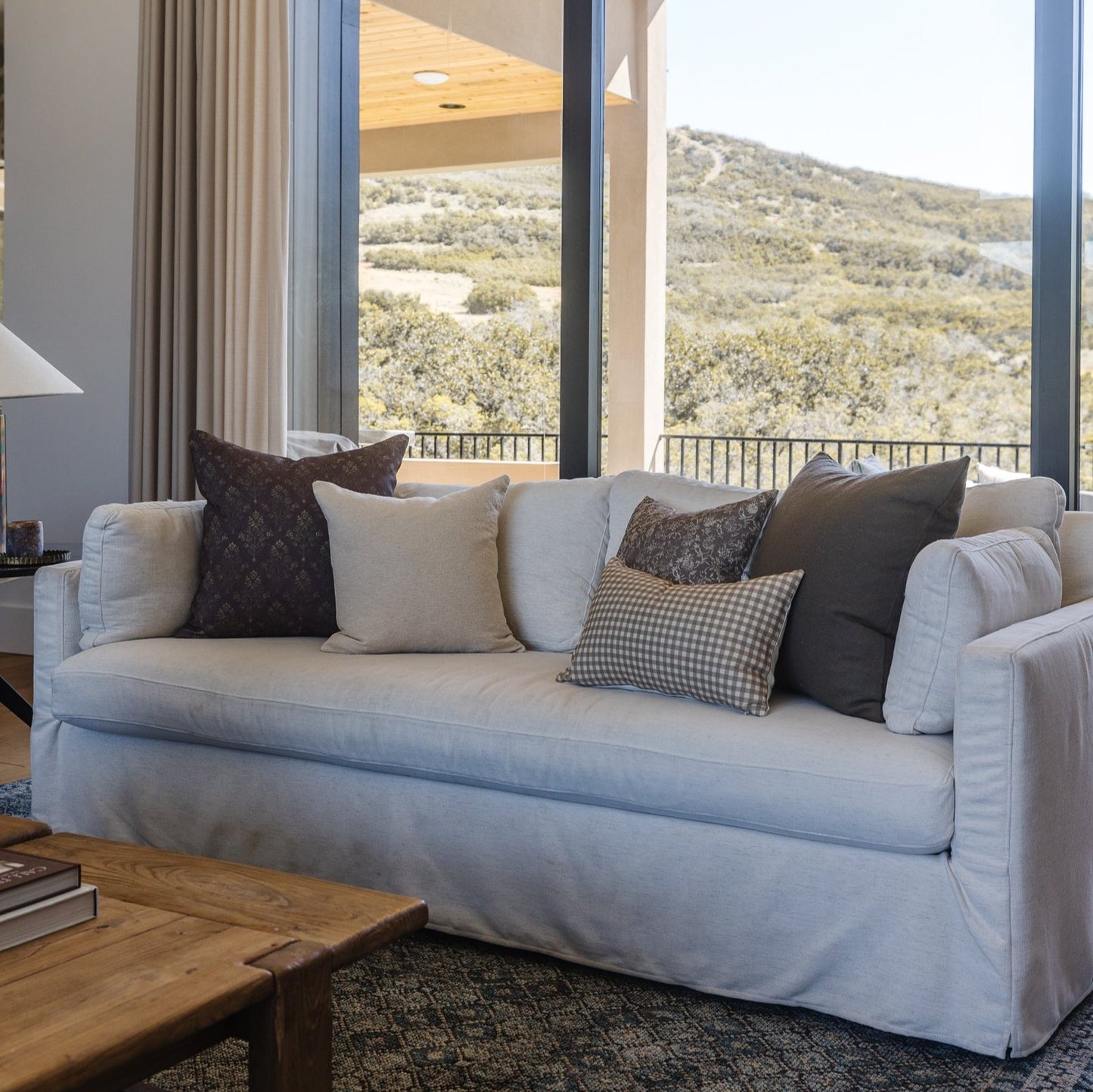Light blue linen sofa with rolled arms and skirted base, styled with multiple decorative pillows in neutral and dark tones.