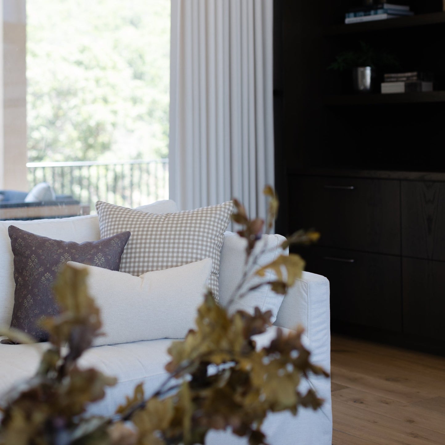 Dark burgundy linen pillow displayed on white sofa with patterned pillows in bright living room.