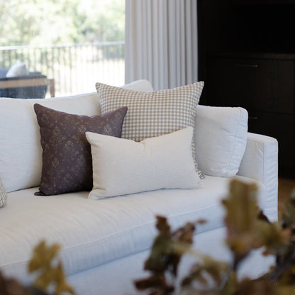 Tan and white gingham patterned pillow displayed on a white sofa with other decorative pillows.