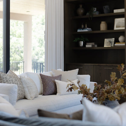 Tan and white gingham patterned square pillow displayed on a cream sofa with coordinating throw pillows.