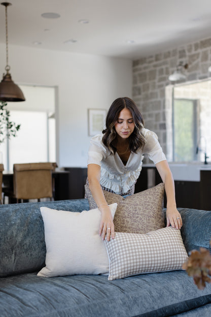 Off-white boucle textured pillow displayed on a blue sofa alongside patterned pillows in a modern living room.